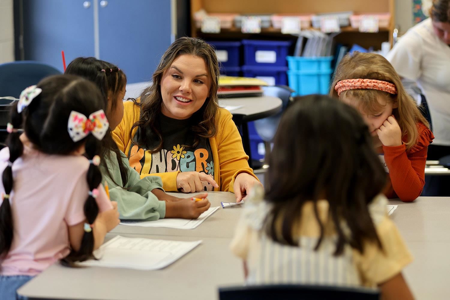 Kindergarten teacher at West Lawn Elementary smiling at a table with students showing them their worksheet.